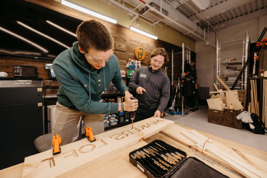 Guy drilling out the lettering for Maker's Loft with the assistance of a maker mentor